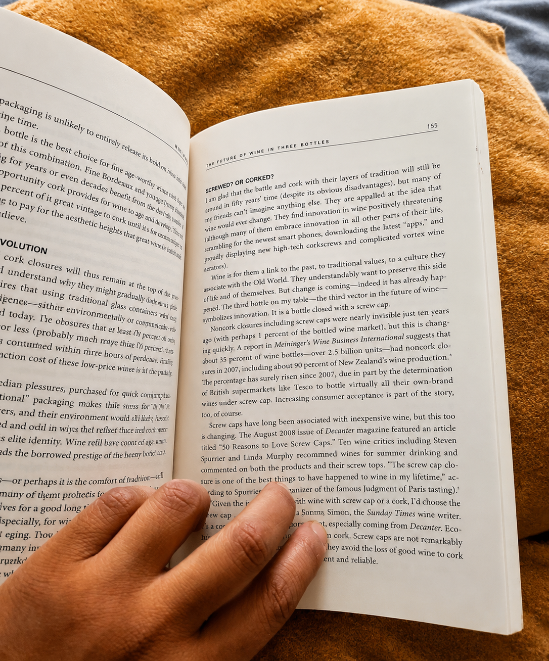 An open wine book resting on a mustard blanket, held open by a hand
