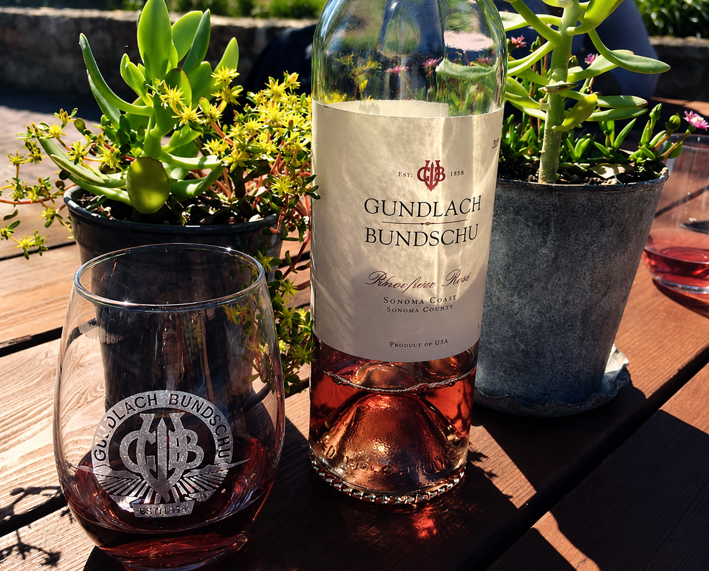 A bottle of Gundlach Bundschu rosé beside a filled glass on a sunlit table