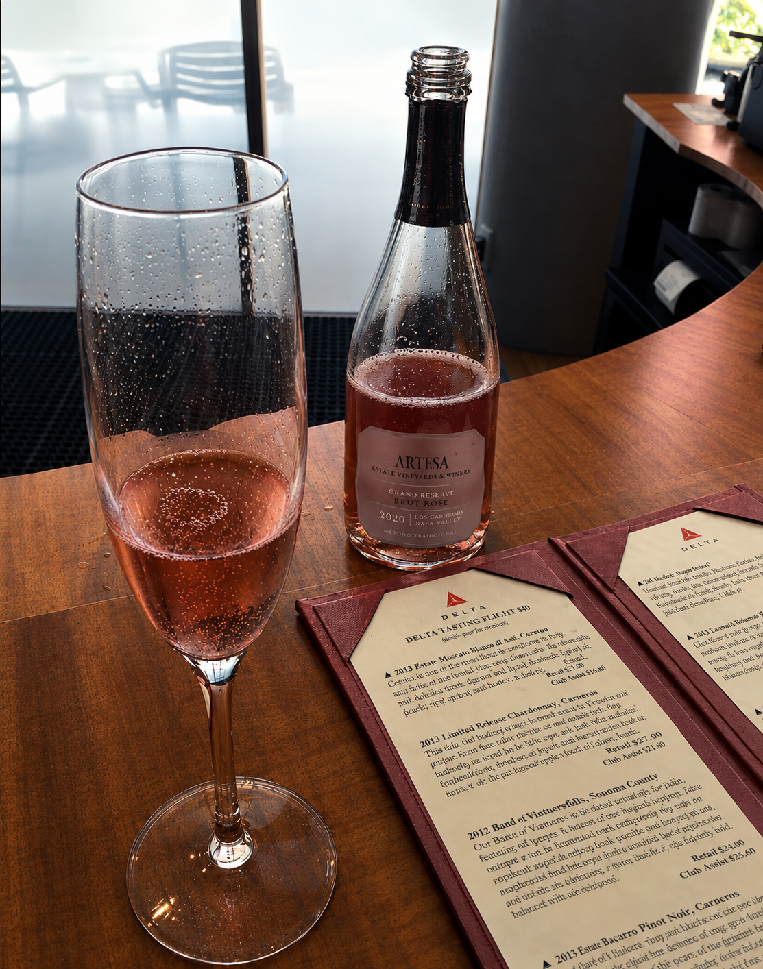 A flute of sparkling rosé beside a small bottle of rosé prosecco on a polished bar top