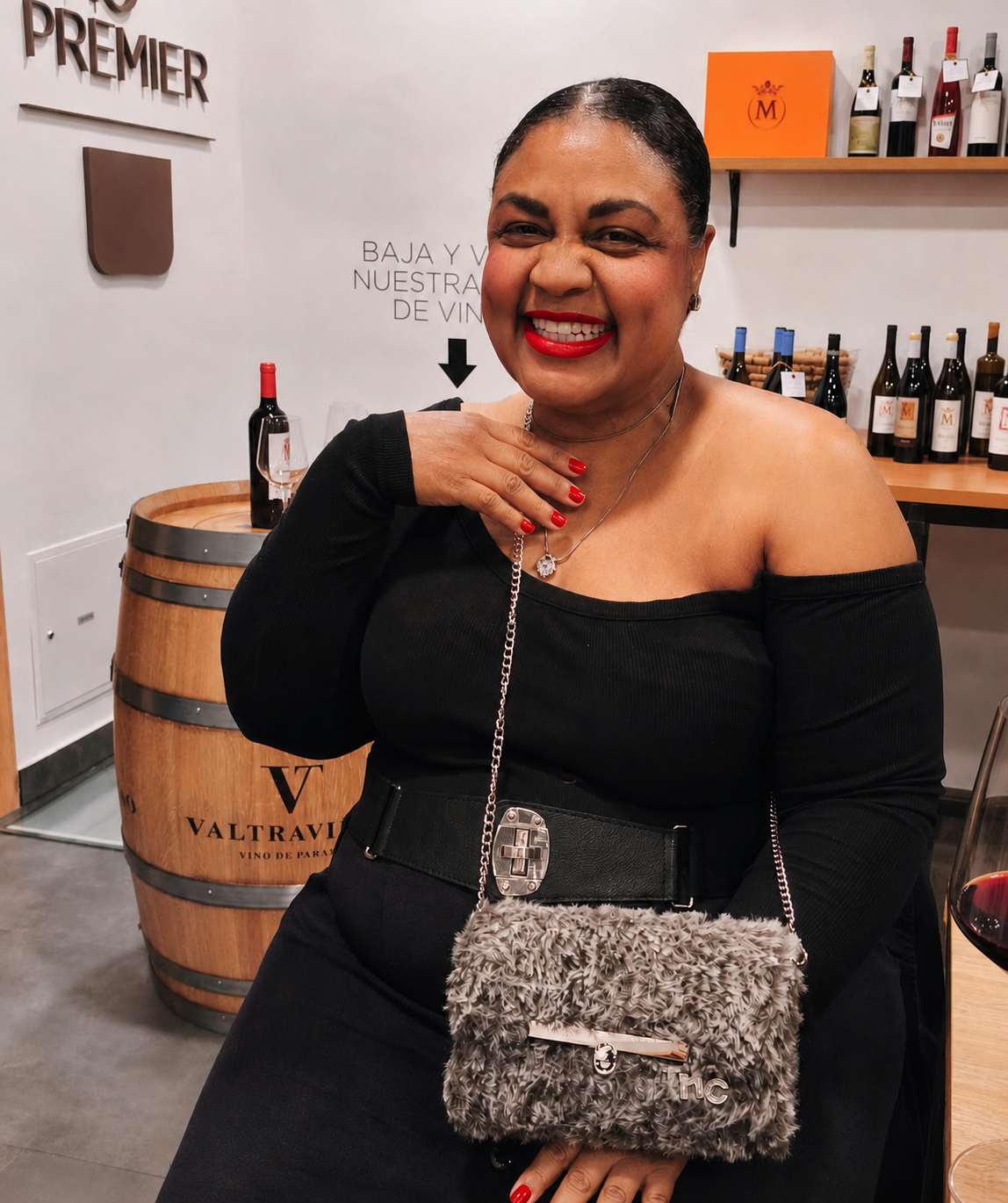 Vinlore founder seated in a wine tasting room beside a wooden barrel, holding a fur bag with a chain strap